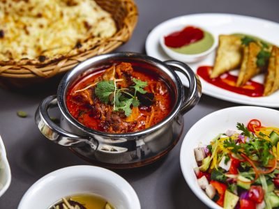 side lamb ragout with fried onion carrot tomato sauce greens and vegetable salad on the table